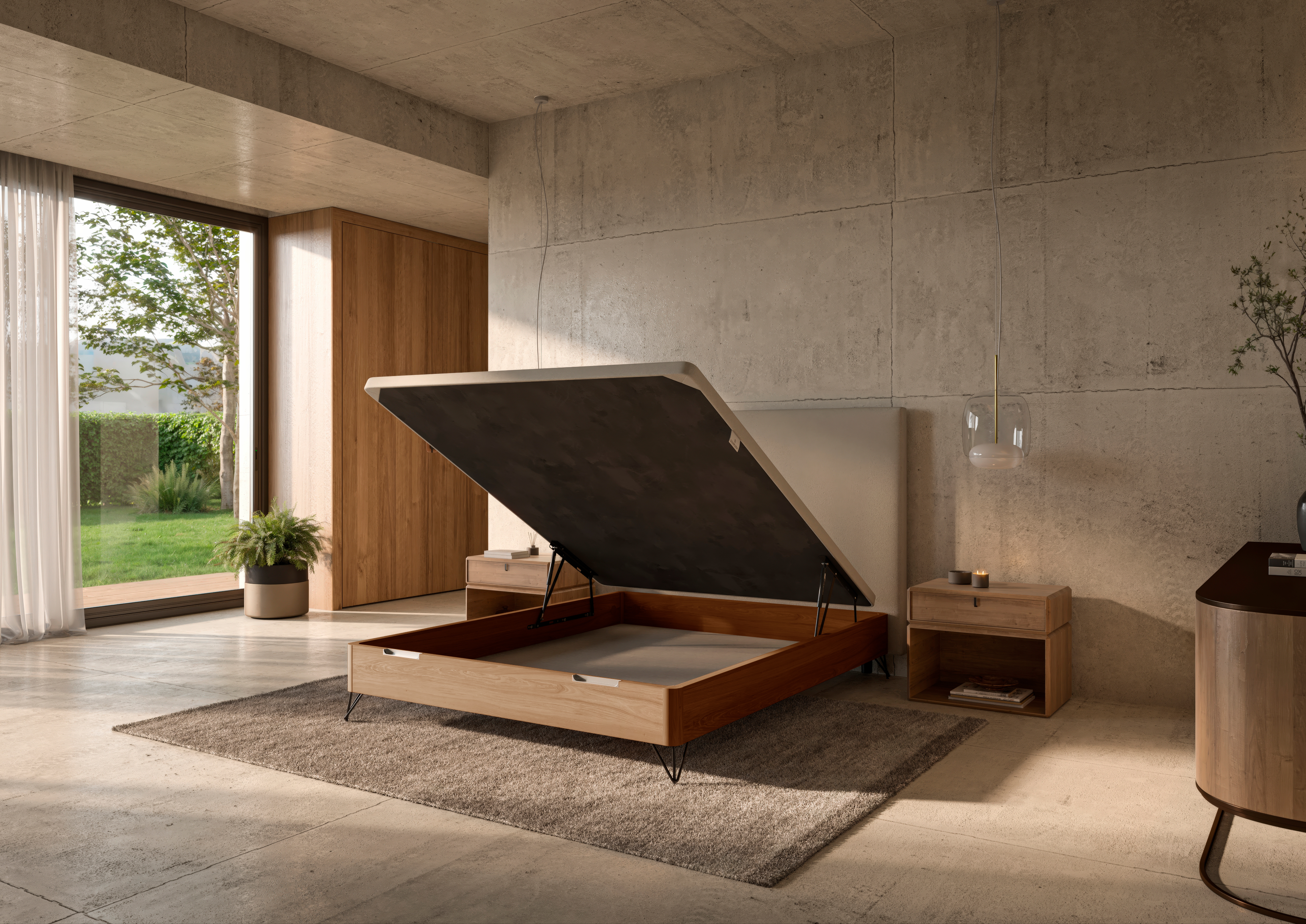 Escena de dormitorio moderno con un canapé abatible levantado mostrando el espacio de almacenamiento, con estructura de madera, cabecero tapizado en gris y mobiliario minimalista